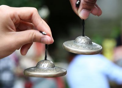 A close up of two hands, each holding an ornament attached to some string.