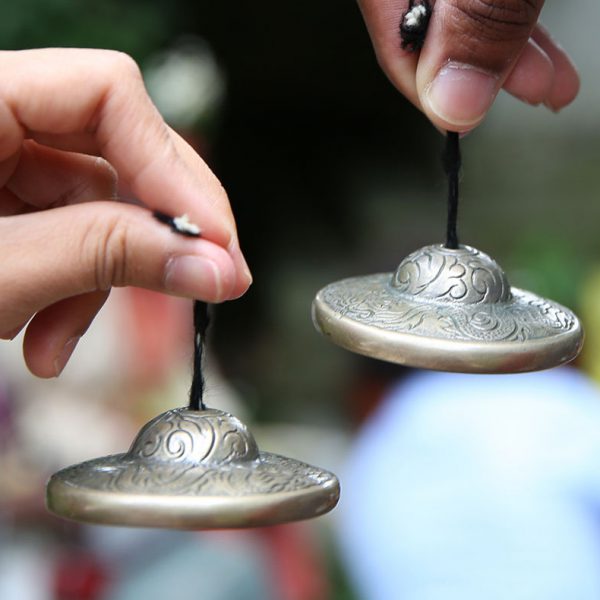 A close up of two hands, each holding an ornament attached to some string.