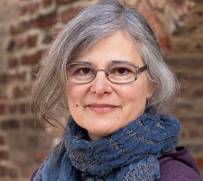 A portrait of Rebecca, with her hair tied up, wearing a blue scarf