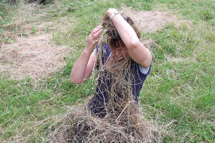 A woman in a field covering herself in hay