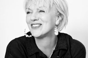 Black and white portrait of Rachel, a white woman with short white hair, smiling