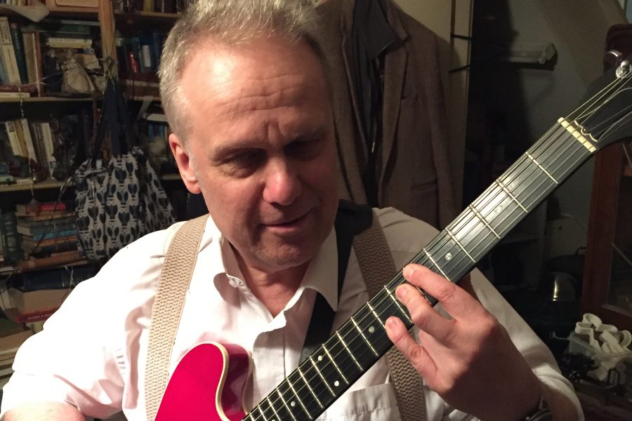 Portrait of Rikki, a white man with grey hair, playing guitar