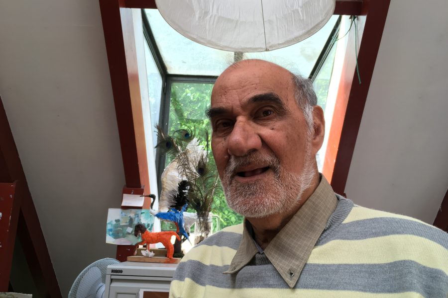 Portrait of Kurban Haji, a man with short grey hair wearing a yellow and grey striped top