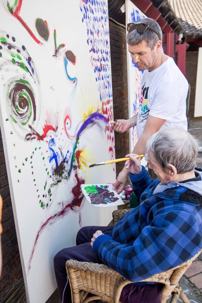 man painting large painting with man helping