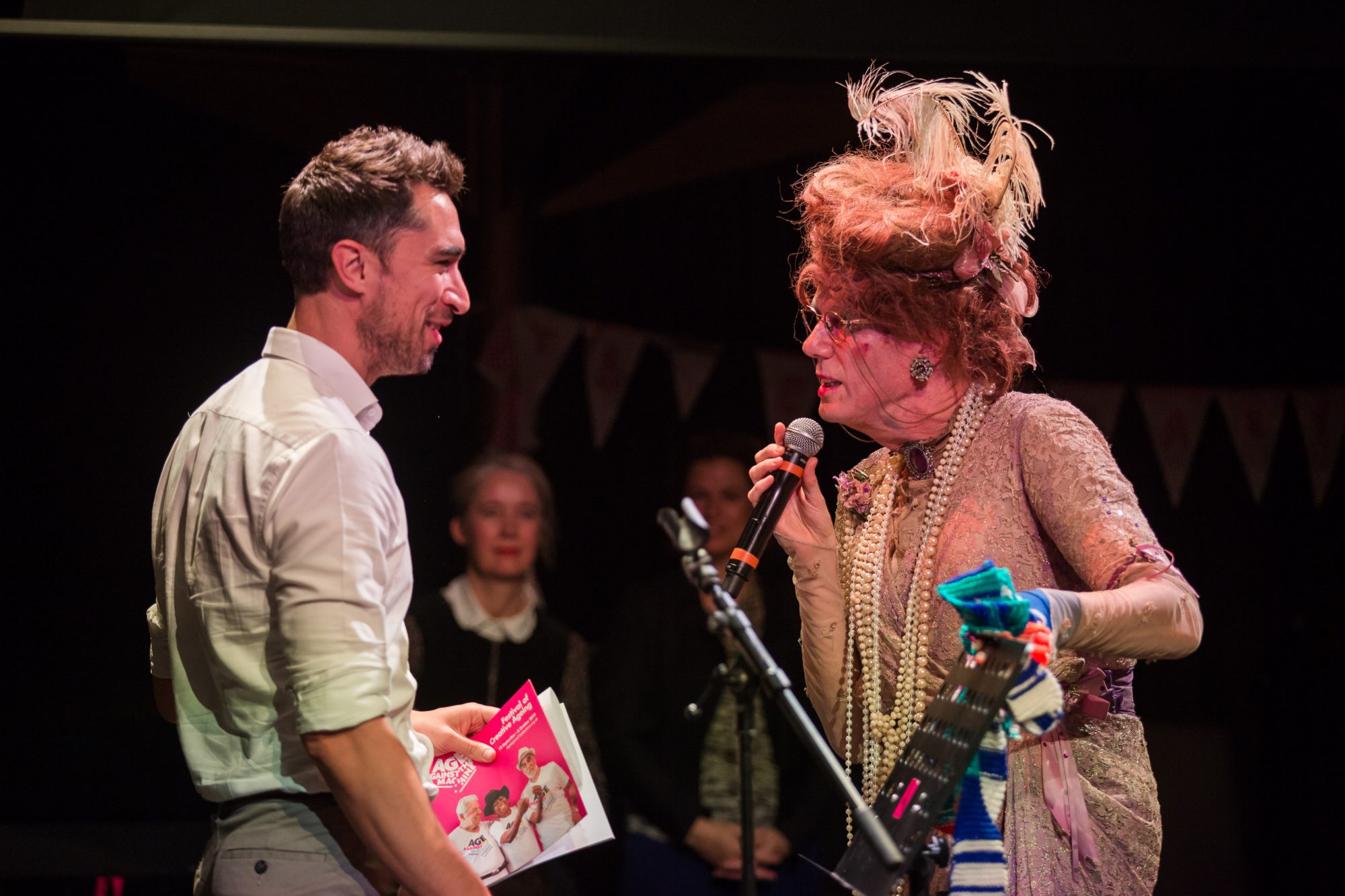 man dressed as woman talking to a man on stage