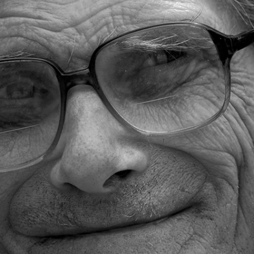 close up of a mans face with glasses, he is smiling