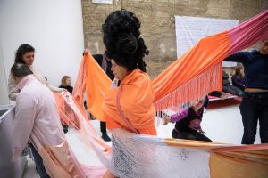 man dressed in large curly black wig with fabrics draped from the ceiling
