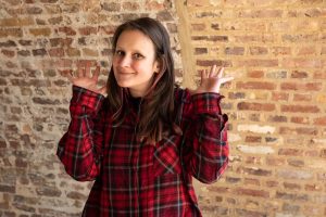 Portrait of Roxanna, a woman with long brown hair, with her hands up