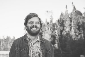 Portrait of a man with dark hair and beard and glasses, smiling