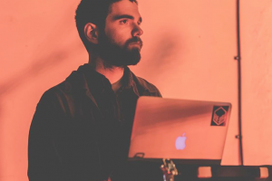 Man with short dark hair and beard making music on a computer