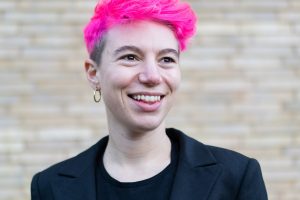 portrait of Lily Ash Sakula, a white person with short, dyed pink hair