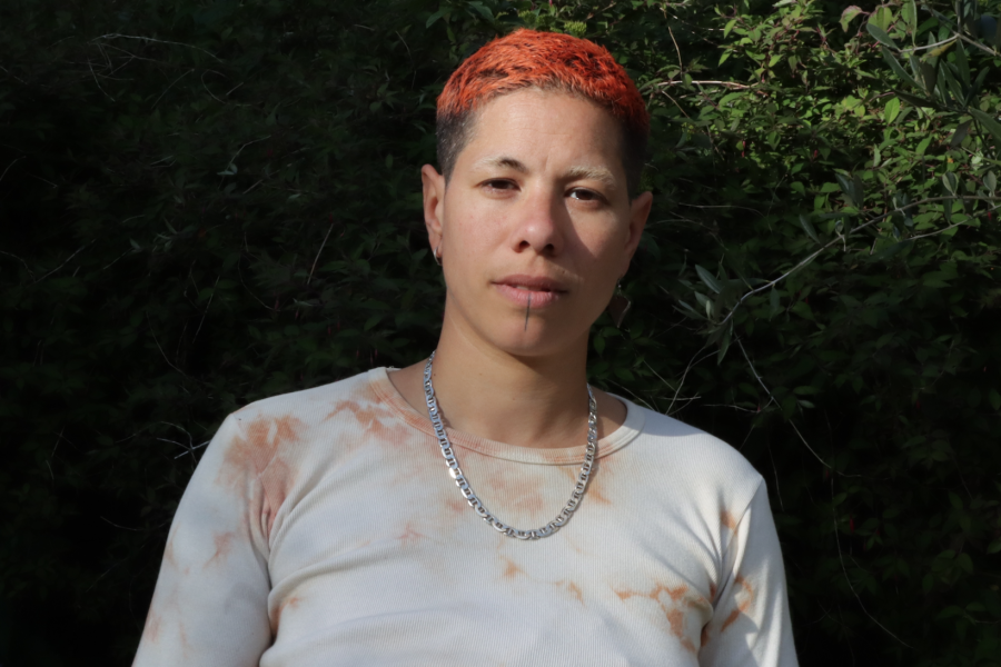 A person with dyed red hair wearing a light coloured top and a chain necklace