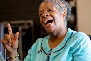portrait of a smiling black woman in turquoise cardigan with a head scarf.
