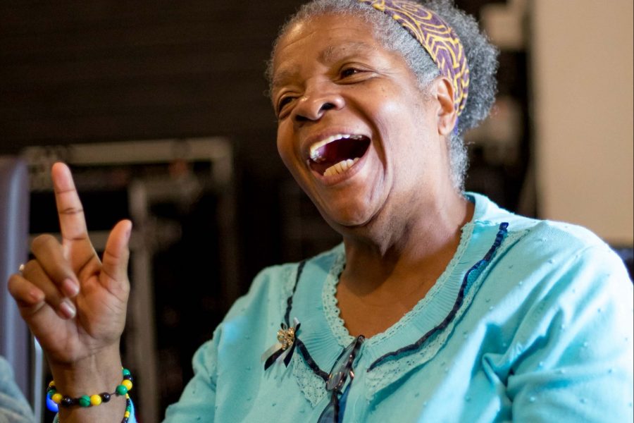 portrait of a smiling black woman in turquoise cardigan with a head scarf.