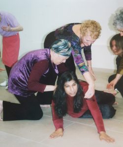a women crouched on the floor being looked at and moved by 5 people