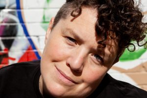 A white woman with short curly brown hair smiling at the camera