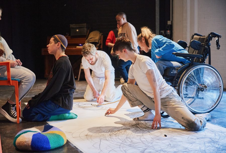 A group of people drawing on a large sheet on paper on the floor.