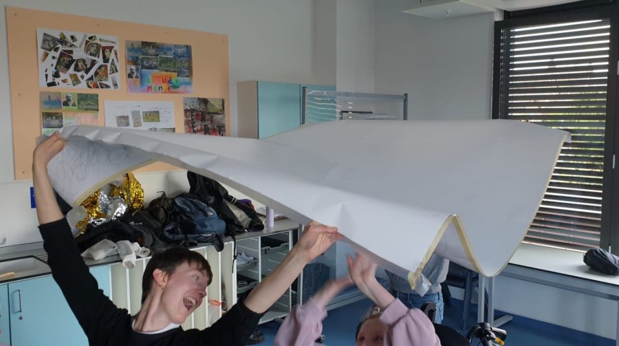 People smiling and holding a large sheet of white paper above their heads